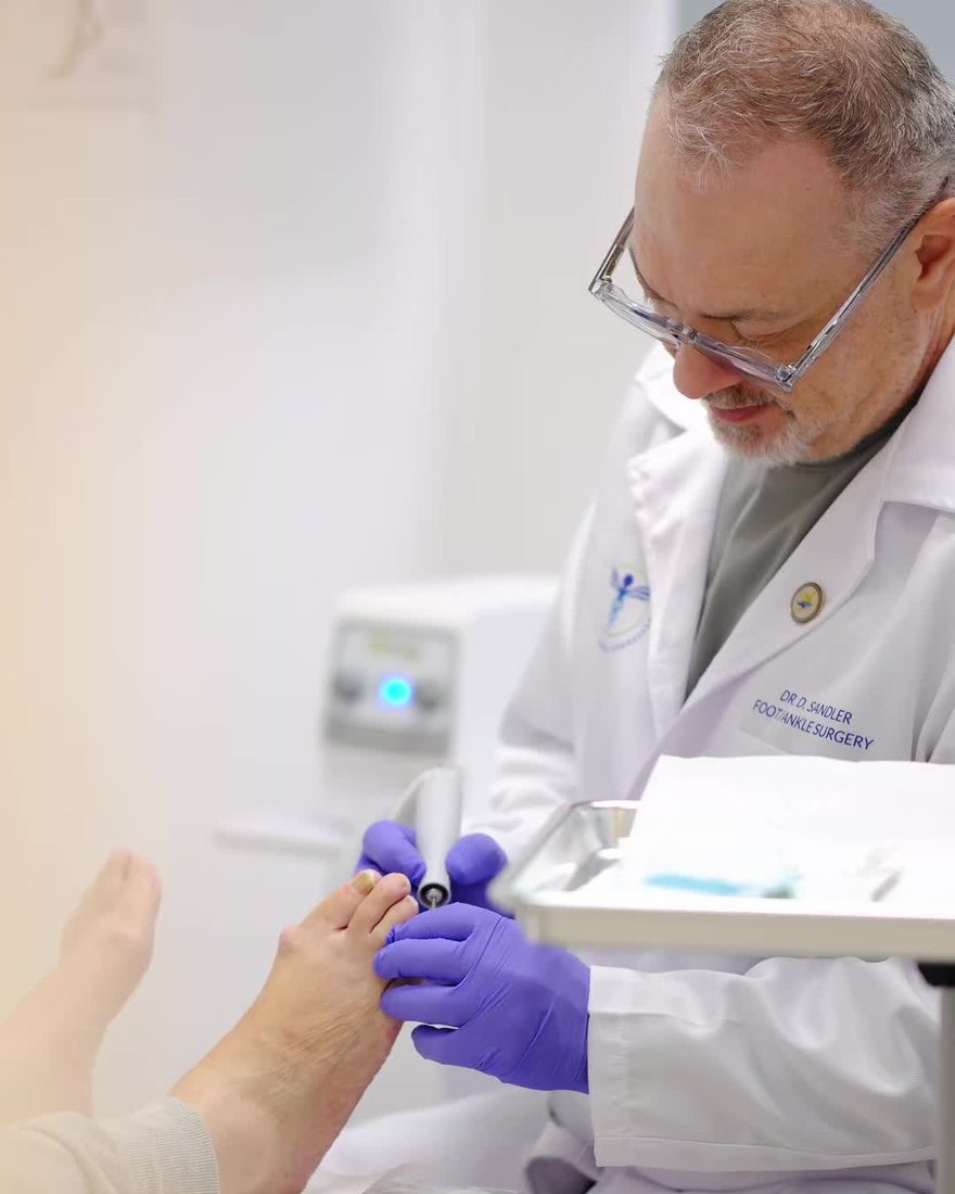 Dr. Dmitry Sandler thinning a patient's toenail with a handheld instrument at Skylake Medical Associates